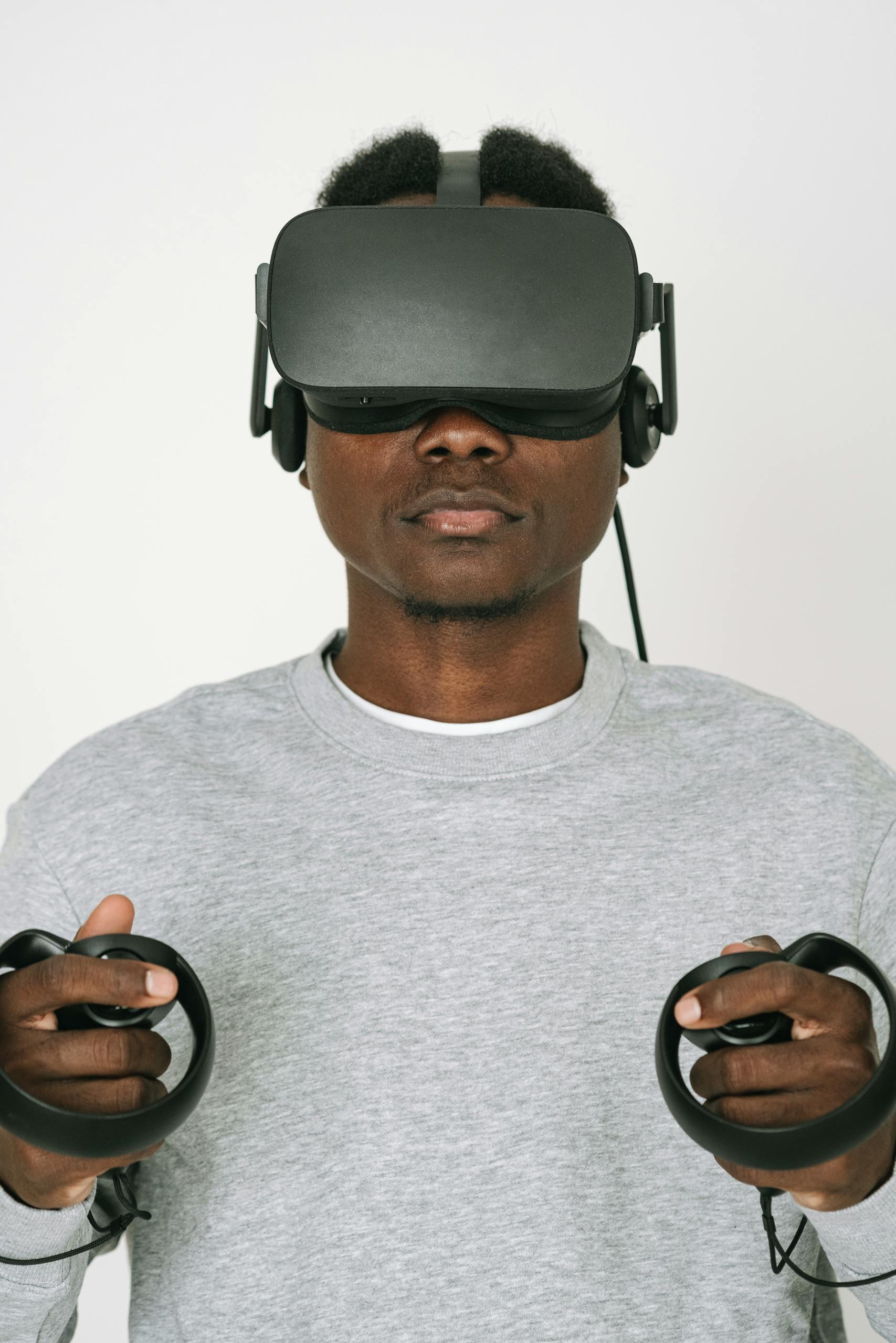 A man wearing VR glasses and gray sweater interacts with virtual reality controllers on a white background.AI With ACE Spencer
